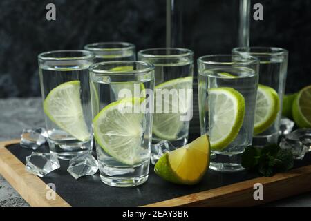 Board with bottle and shots of vodka with lime on gray table Stock Photo