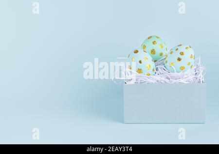 Simple and minimal easter background - easter eggs with golden dots in gift box on blue backdrop. Stock Photo