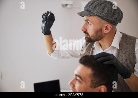 Seriously focused Caucasian barber using special instrument for hair cut in room inddors Stock Photo