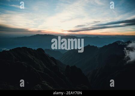 Sun-set moment, scenery of mountains in layers, dark violet purple silhouette panoramic view. Stock Photo