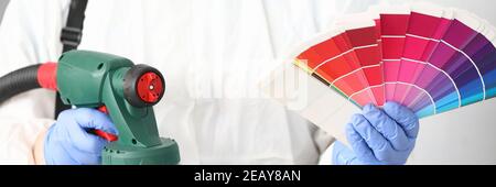 Man holds in his hands spray gun and palette of colors. Stock Photo