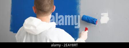 Man with roller in his hands paints wall in blue. Stock Photo