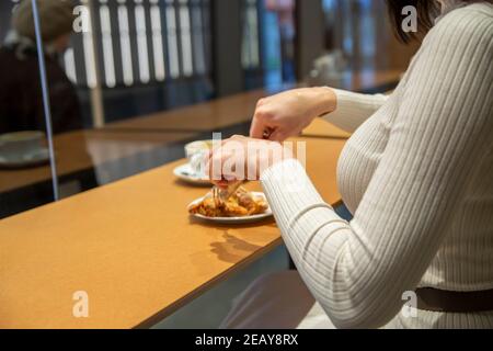 woman cuts croissant and drinks coffee at a table in a cafe. no face Stock Photo