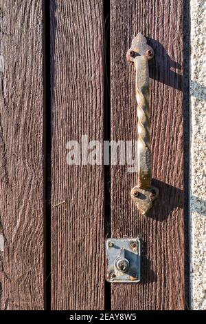 Old plank door with an ancient rusty iron ornamental handle and a peeling keyhole. Rusty screws. Vintage concept Stock Photo
