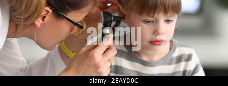 Woman otorhinolaryngologist examines little girl's ear with otoscope in clinic Stock Photo