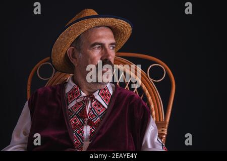 Nice portrait of Ukrainian country-man sitting in a wicker chair, wearing straw hat and traditional clothes (Vyshyvanka) Stock Photo