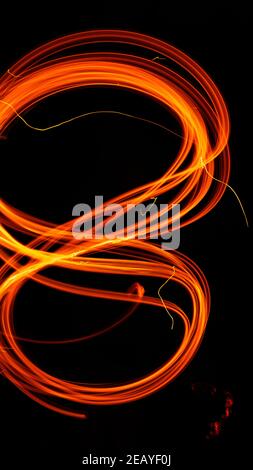 Drawing shapes with fire at night, infinity sign, bright colors on night background, fun with fire. Abstract fiery pattern in the shape of the number Stock Photo