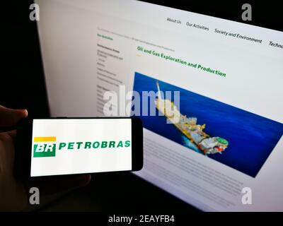 Person holding smartphone with logo of petroleum company Petróleo Brasileiro S.A. (Petrobras) on screen in front of website. Focus on phone display. Stock Photo