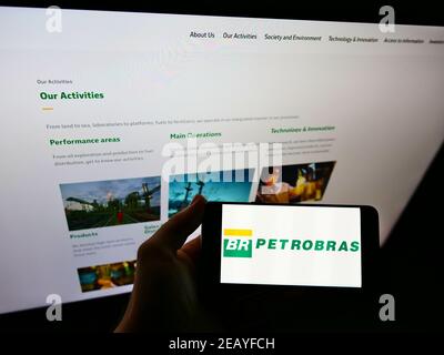Person holding mobile phone with logo of petroleum company Petróleo Brasileiro SA (Petrobras) on screen in front of web page. Focus on phone display. Stock Photo