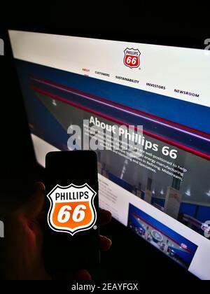 Person holding mobile phone with logo of American oil and gas business Phillips 66 Company on screen in front of web page. Focus on phone display. Stock Photo