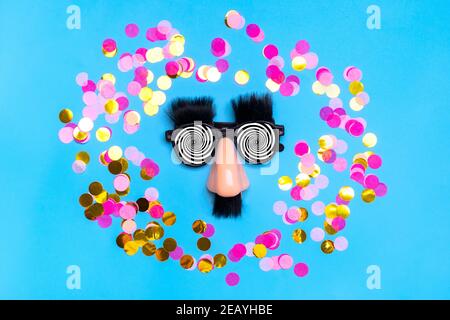 funny face - fake eyeglasses, nose and mustache, confetti, sequins on blue background Happy fools day concept 1st April party Holiday card Stock Photo