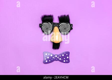 funny face - fake eyeglasses, nose and mustache, confetti, sequins on purple background Happy fools day concept 1st April party Holiday card Stock Photo