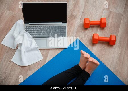 Towel dumbbells laptop Top view. Young woman do fitness workout, stretching exercises using laptop via videocall. Woman in sportswear make remote yoga Stock Photo