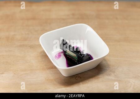 A clogged printhead from an inktjet printer being washed in a white bowl. Diy repairing and maintaining electronic devices Stock Photo