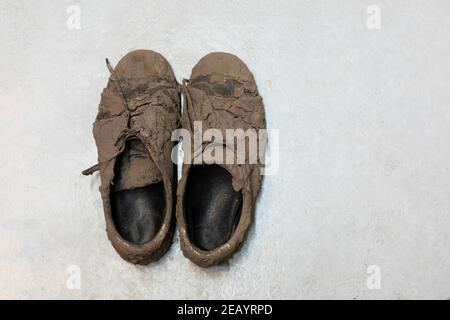 Dirty dried muddy messy sneaker shoes totally covered with mud looking unrecognizable while laying on the floor Stock Photo