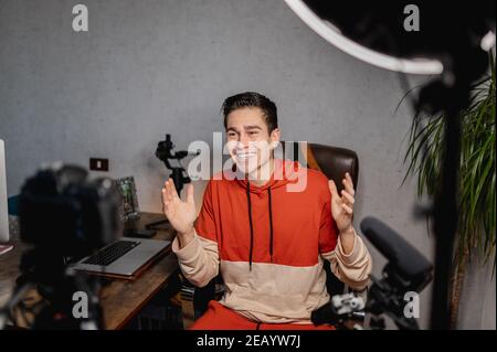 Young man sitting at the desk talking to the camera. Guy recording a video with professional equipments. Vlog, freelancer concept. Stock Photo