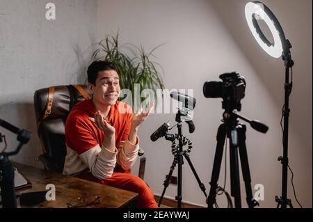 Young man sitting at the desk talking to the camera. Guy recording a video with professional equipments. Vlog, freelancer concept. Stock Photo