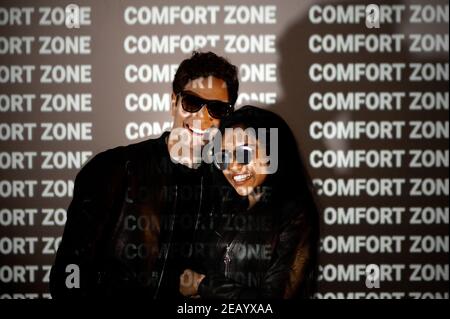 Side view of Indian Caucasian couple in stylish clothes with sunglasses standing on black background and illuminated by light of projector with words Stock Photo