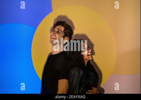 Indian and Caucasian couple with leather black jacket smiling standing back to back looking at opposite side. Colorful background in studio illuminate Stock Photo