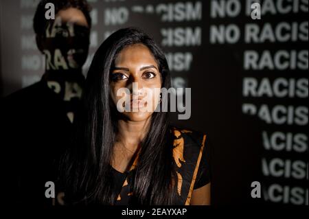 Indian young woman in traditional dress looking at the camera with serious face. Unrecognizable white man back to her. Discrimination and violence aga Stock Photo