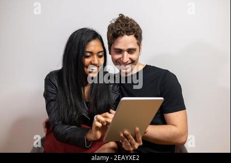 Young smiling couple using tablet sitting on armchair at home. Stock Photo