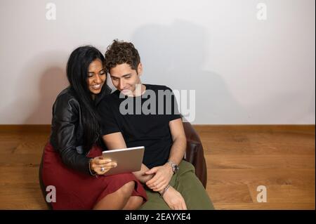 Young smiling couple using tablet sitting on armchair at home. Stock Photo