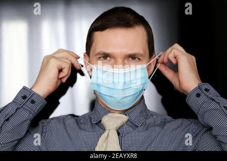 Man in office clothes puts on medical face mask. Concept of safety measures during coronavirus pandemic Stock Photo