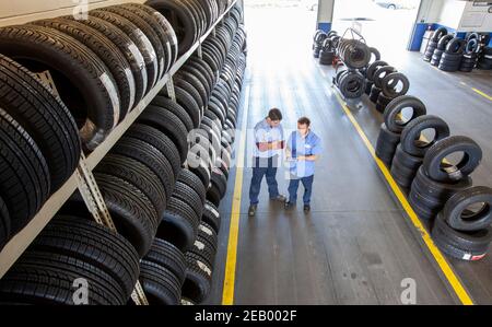 Two mechanics working the tire area of an auto repair shop, using a digital tablet Stock Photo