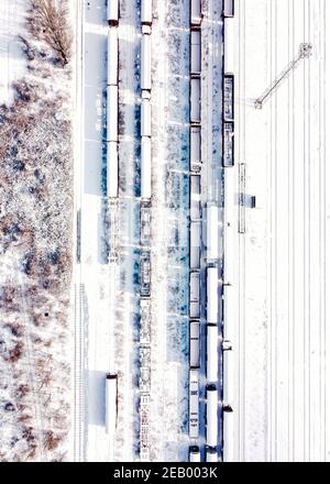 Top view of cargo trains. Aerial view from flying drone of snow covered freight trains on the railway station. Wagons with goods on railroad. Stock Photo