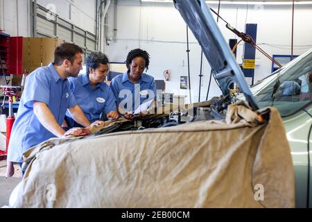 Three mechanics sharing a digital tablet and planning work on a car in for repair Stock Photo