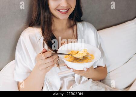 cornflakes for breakfast in bed. beautiful woman holding a plate of cornflakes while she is lying on the bed Stock Photo