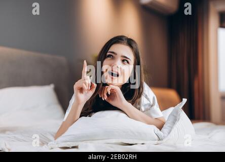 Young beautiful woman has an idea while she is lying on the bed. The female model shows emotions Stock Photo