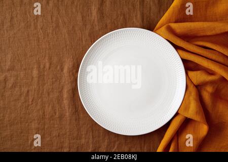 Clean empty white plate, fork and knife on bright dark brown tablecloth on table, yellow mustard napkin Stock Photo
