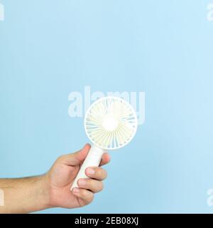 Man holding small portable usb fan close-up isolated on blue background. Space for text Stock Photo