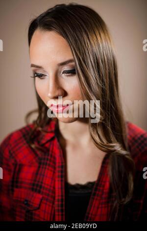 Portrait of a female looking down and sideways thinking about something on a brown background Stock Photo
