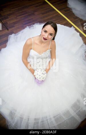 Vertical shot of a bride sitting on the wooden floor making her wedding gown spread Stock Photo