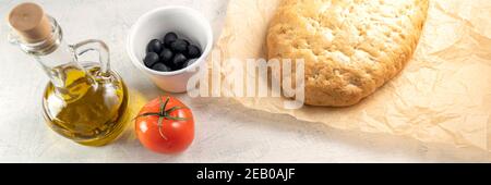 Banner with Italian focaccia or Italian bread. Fresh, tasty bread with aromatic herbs on wooden board next to tomato, black olives and olive oil with Stock Photo