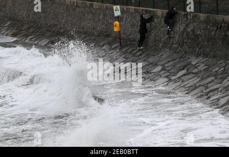 Two man climb a wall to avoid breaking waves along the sea front at Seapoint Beach in Dublin as Met Eireann have issued two weather warnings including strong to gale force southeast winds in conjunction with rain, sleet and snow. Picture date: Thursday February 11, 2021. Stock Photo