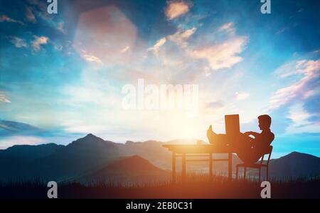 Businessman sitting in the mountains behind the desk with the laptop. Business concept. Stock Photo
