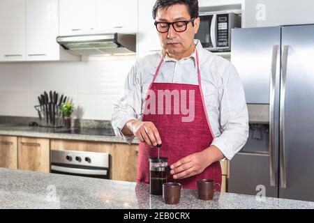 Man in red apron preparing coffee in a French press in kitchen Stock Photo