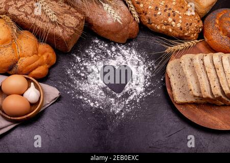 Love cooking. Various of rye bread on a dark background. Copy space for text. Baking background with heart shape and flour and food ingredients on the Stock Photo