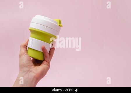 Hand holding reusable cup for coffee on pink background. Stock Photo