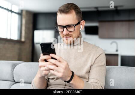 Handsome guy is using smartphone for messaging, texting, a young man in smart casual wear sitting with a phone in the hands, typing a message Stock Photo