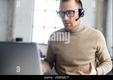 A friendly guy with a headset using laptop for communication with employees, coworkers, video conference. A support officer is talking with a Stock Photo