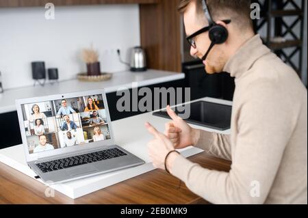 Back view on the laptop screen with a many diverse people on it, a guy with a headset using computer app for communication with employees, coworkers Stock Photo