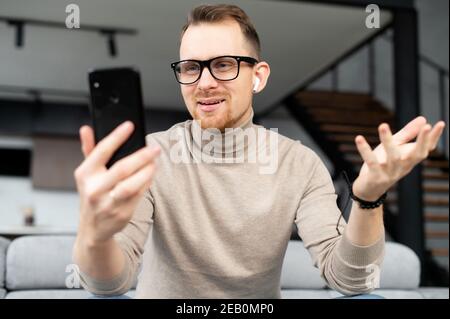 A young handsome man wearing eyeglasses using a smartphone for video chat, video call. A smiling guy is talking online via video connection on the Stock Photo
