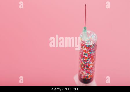 Medical Syringe filled with colorful balloons on a pink background with free space. Conceptual medical vaccine development. Stock Photo