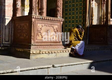 Pushkar, Rajasthan, India - December 2016: Indian man sitting on the floor and reads newspaper. Hindu near the temple with decorative walls Stock Photo