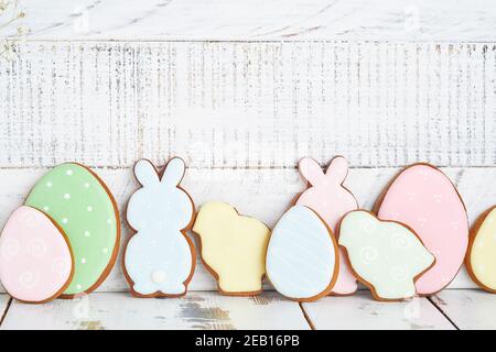 Easter greeting card with colorful rabbits, eggs, chickens and carrots gingerbread cookies on white wooden old background with copy space. Mock up. Ba Stock Photo