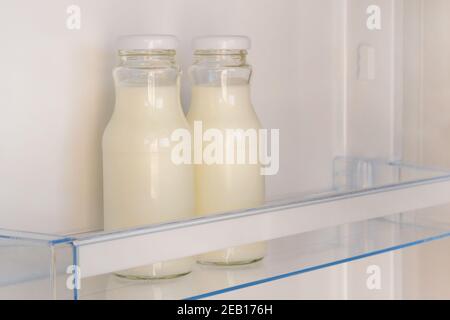Yogurt in white bottles on shelf of open empty fridge. Weight loss diet concept. Fermented food. Stock Photo